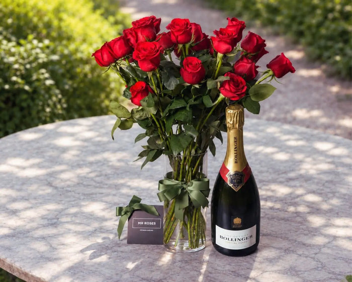 Long stem red roses in a glass vase beside a bottle of Bollinger Special Cuvée champagne