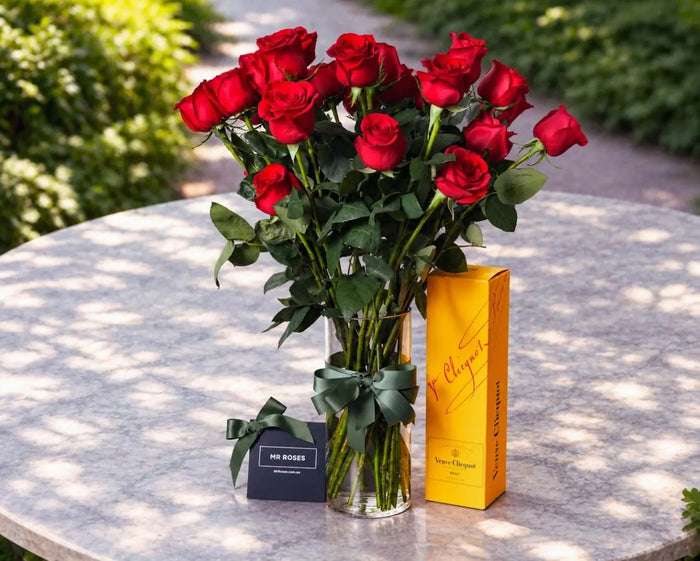 Long stem red roses in a glass vase beside a Veuve Clicquot champagne gift box