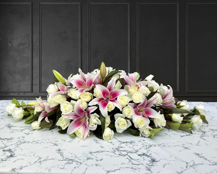 funeral spray of white roses and pink lilies, funeral flowers and casket flowers in white